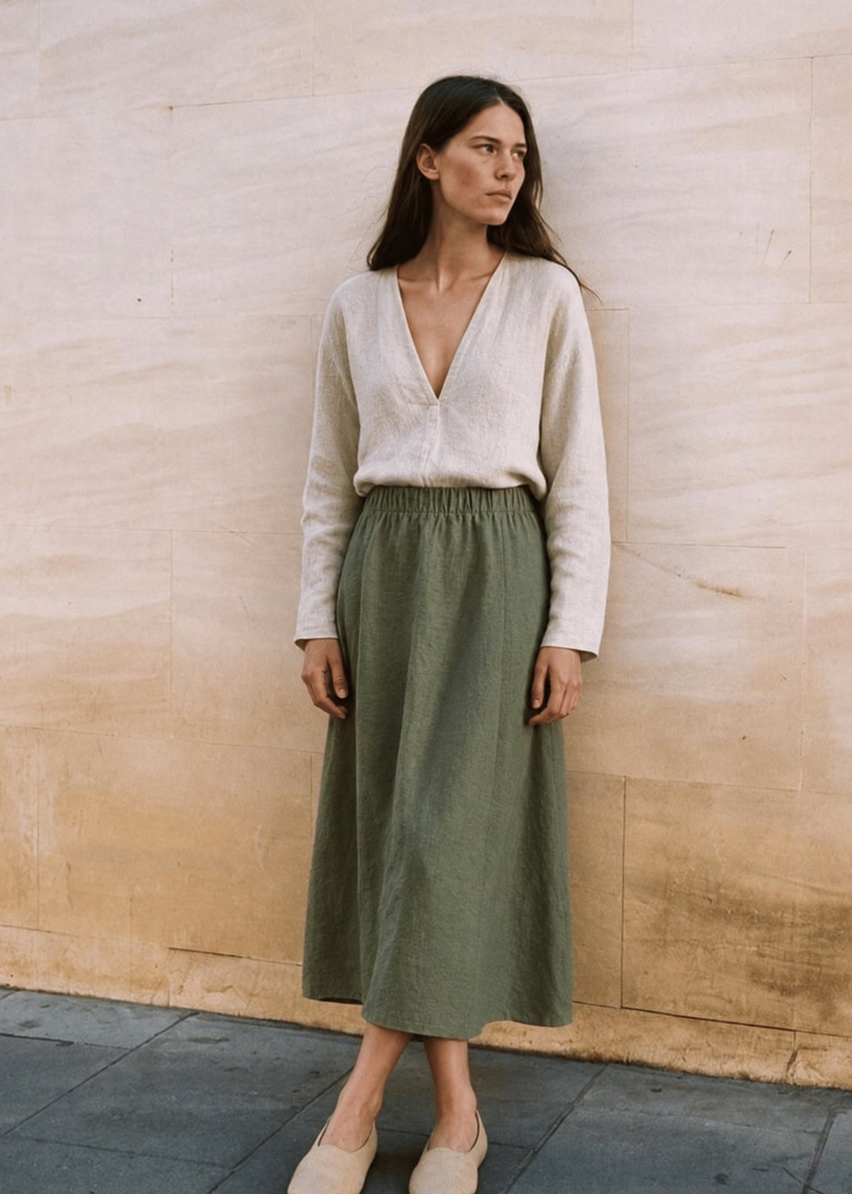 Woman standing against a stone wall in the olive A-Line Paneled Skirt with an elastic waistband.