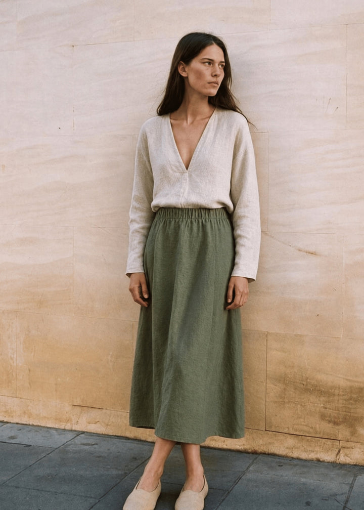Woman standing against a stone wall in the olive A-Line Paneled Skirt with an elastic waistband.