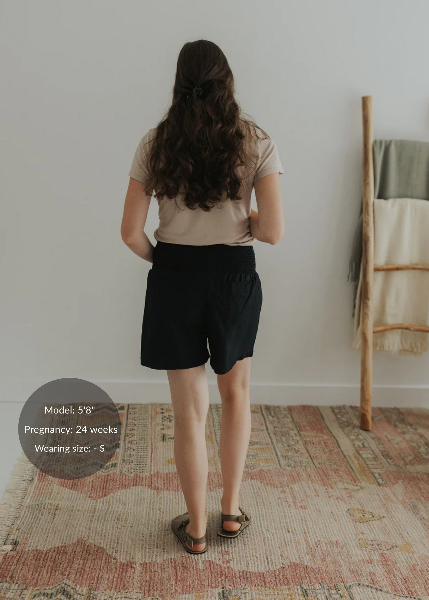 Woman from behind wearing black smocked linen shorts and a beige top.