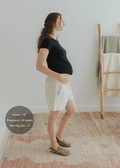 Pregnant woman in natural linen smocked shorts, black tee, and brown sandals.