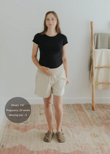 Pregnant model in smocked natural linen shorts with deep pockets and a black tee.