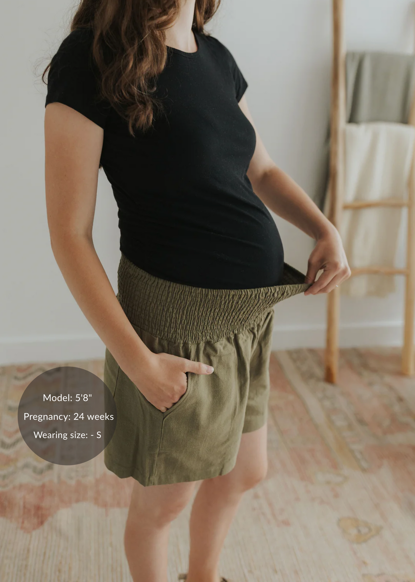 Pregnant woman in olive green smocked linen shorts with deep pockets and a black t-shirt.