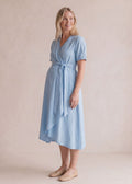 Smiling woman in a light blue adjustable wrap-front midi dress with short sleeves and a waist tie.