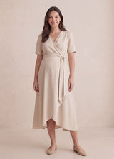 Smiling woman in a beige adjustable wrap front midi dress with short sleeves and a tie waist.
