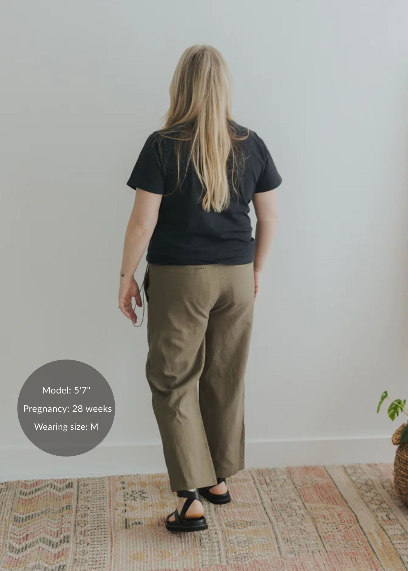 Back view of a pregnant woman in olive cotton/linen side drawstring maternity pants and a black t-shirt.