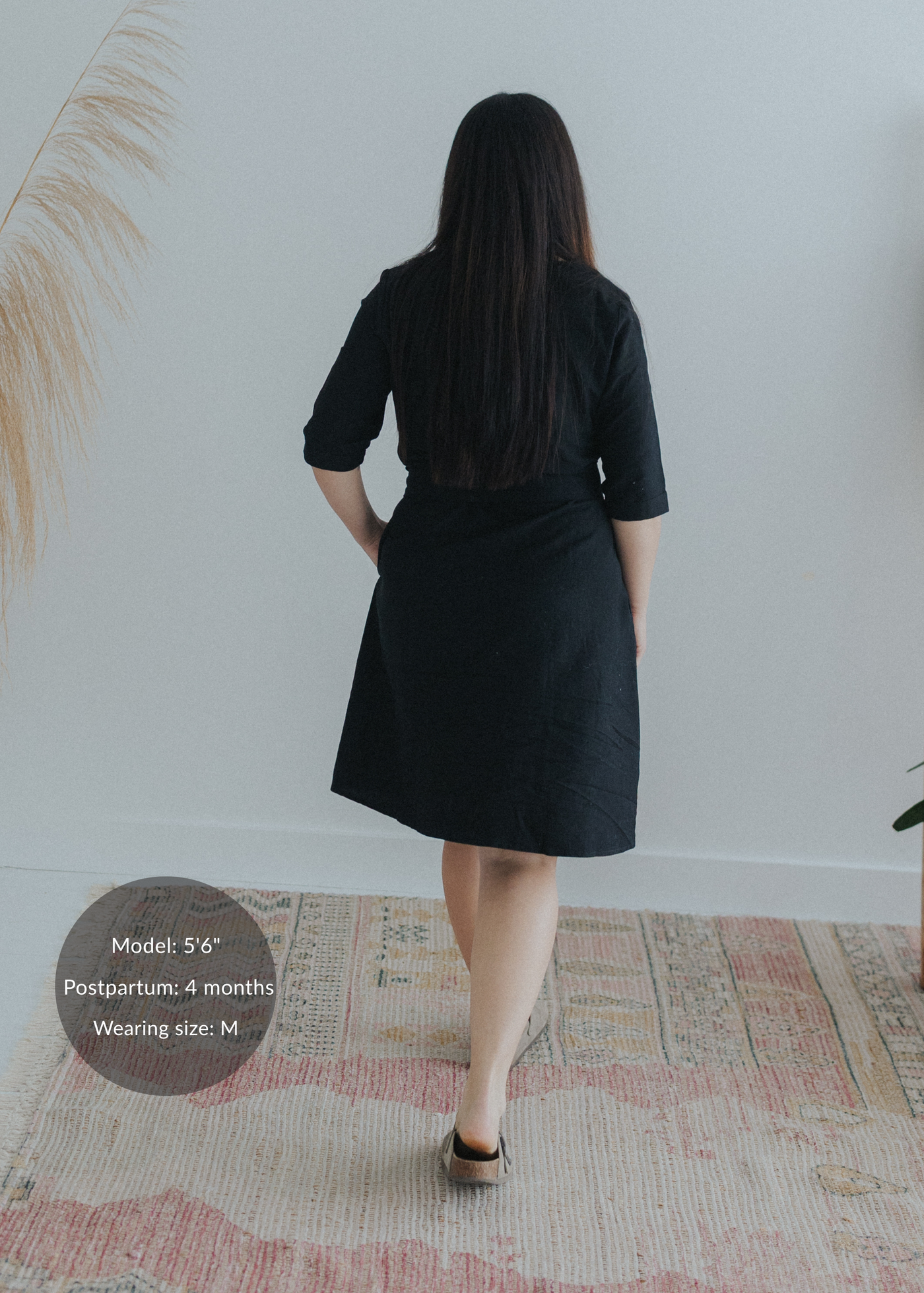 Back view of a woman in a black cotton-linen Willow Dress, knee-length with a flared skirt.