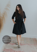 Woman in a black cotton-linen Willow Dress with a button-down front, waist tie, and side pockets.