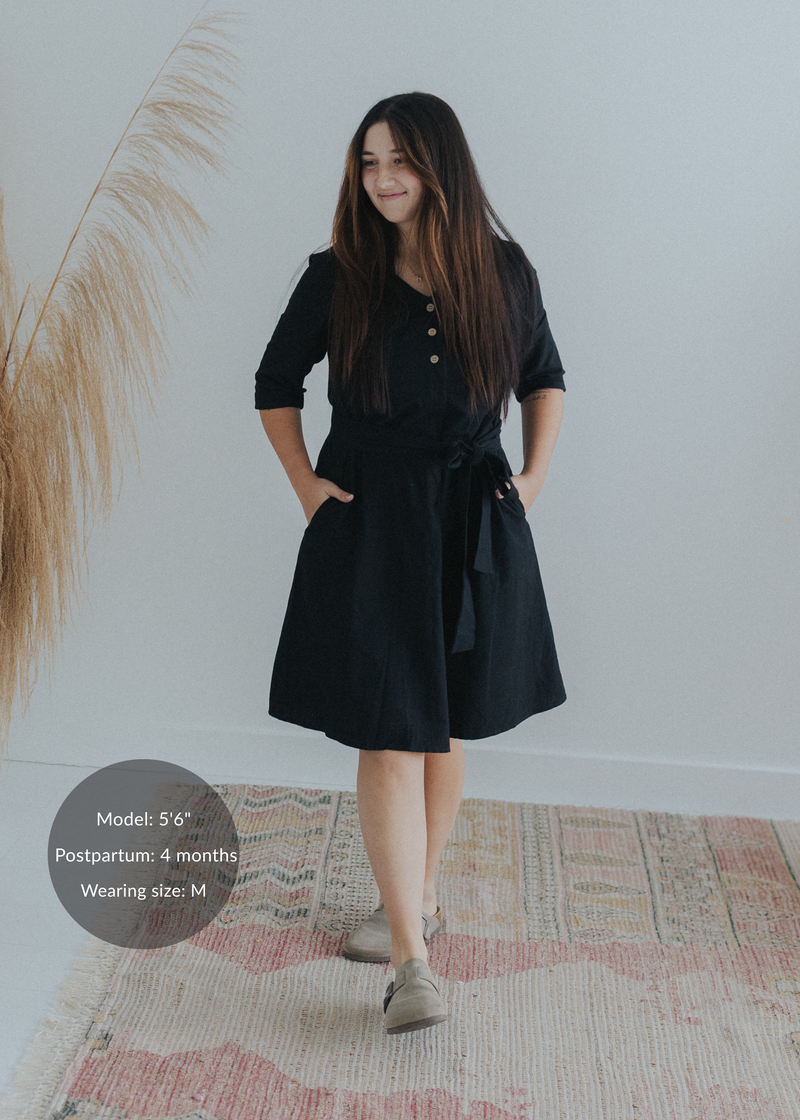 Woman in a black cotton-linen Willow Dress with a button-down front, waist tie, and side pockets.