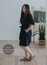Woman in a black cotton-linen Willow Dress with an adjustable waist tie and side pockets, knee-length, flared skirt.