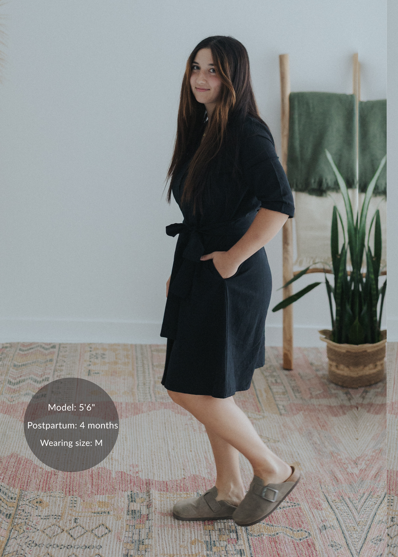 Woman in a black cotton-linen Willow Dress with an adjustable waist tie and side pockets, knee-length, flared skirt.