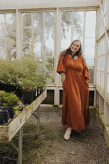 Woman in a rust Eliza Maternity and Nursing Dress in cotton gauze with balloon sleeves and ruffle skirt.