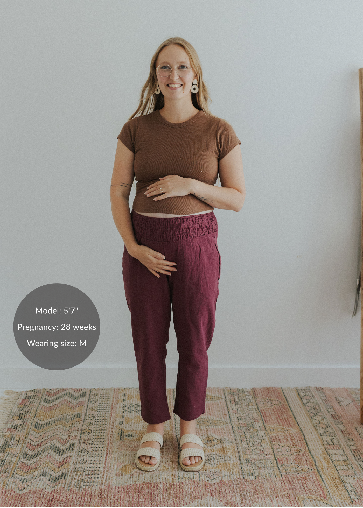 Pregnant woman in smocked waist burgundy linen maternity pants and a brown top.