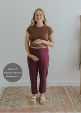 Pregnant woman in smocked waist burgundy linen maternity pants and a brown top.