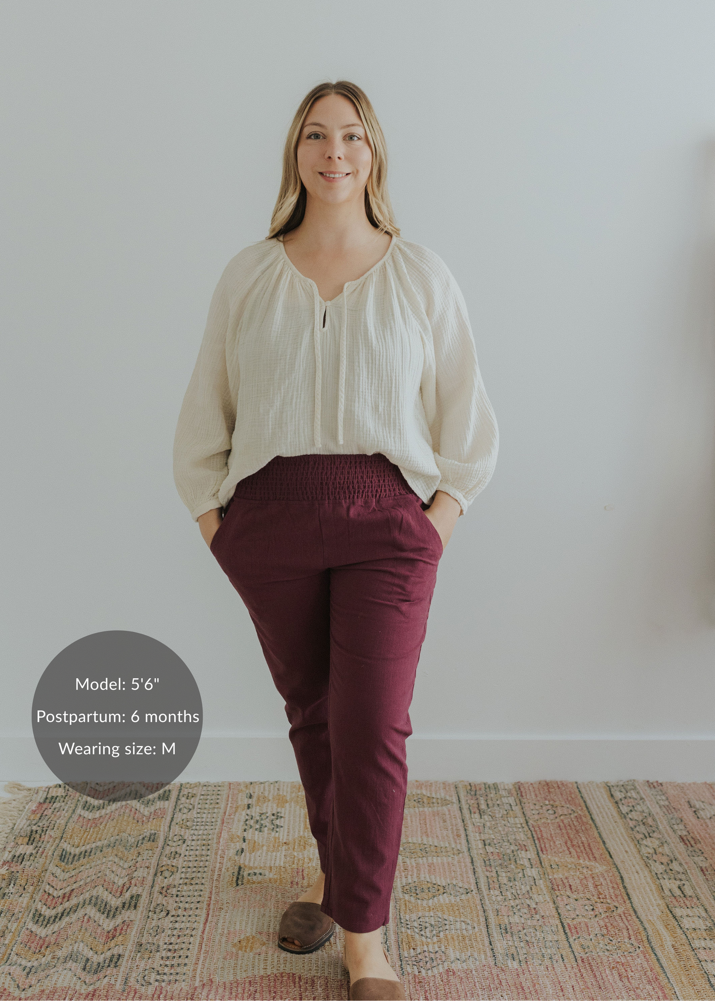 Woman in burgundy smocked linen maternity pants with pockets and an ivory top.