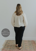 Woman from behind wearing black smocked linen pants and a cream top, with brown sandals.
