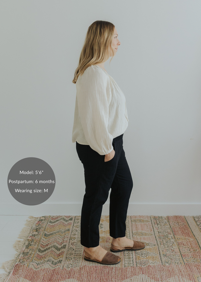 Woman in black smocked linen pants with pockets and an off-white blouse, standing on a patterned rug.