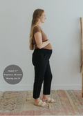 Pregnant woman in black smocked linen maternity pants, brown top, and woven sandals.