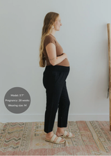 Pregnant woman in black smocked linen maternity pants, brown top, and woven sandals.
