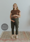 Pregnant woman in olive green smocked linen pants and brown top, smiling.