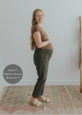Pregnant woman in olive green smocked linen pants with pockets, brown top, and cream sandals.