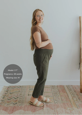 Pregnant woman in olive green smocked linen pants with pockets, brown top, and cream sandals.