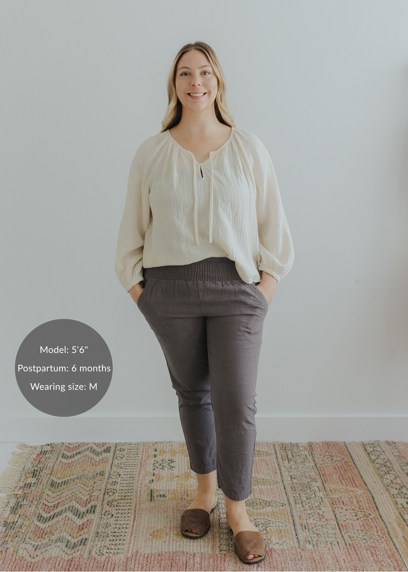 Woman in charcoal smocked linen maternity pants with pockets and an ivory blouse.