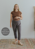 Pregnant woman in charcoal gray smocked linen pants and a brown top, smiling.