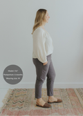 Woman in charcoal smocked linen maternity pants with pockets, paired with a cream blouse and brown flats.