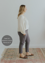Woman in charcoal smocked linen maternity pants with pockets, paired with a cream blouse and brown flats.