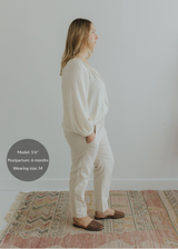 Woman in natural linen smocked pants with pockets, paired with a cream blouse and brown flats.