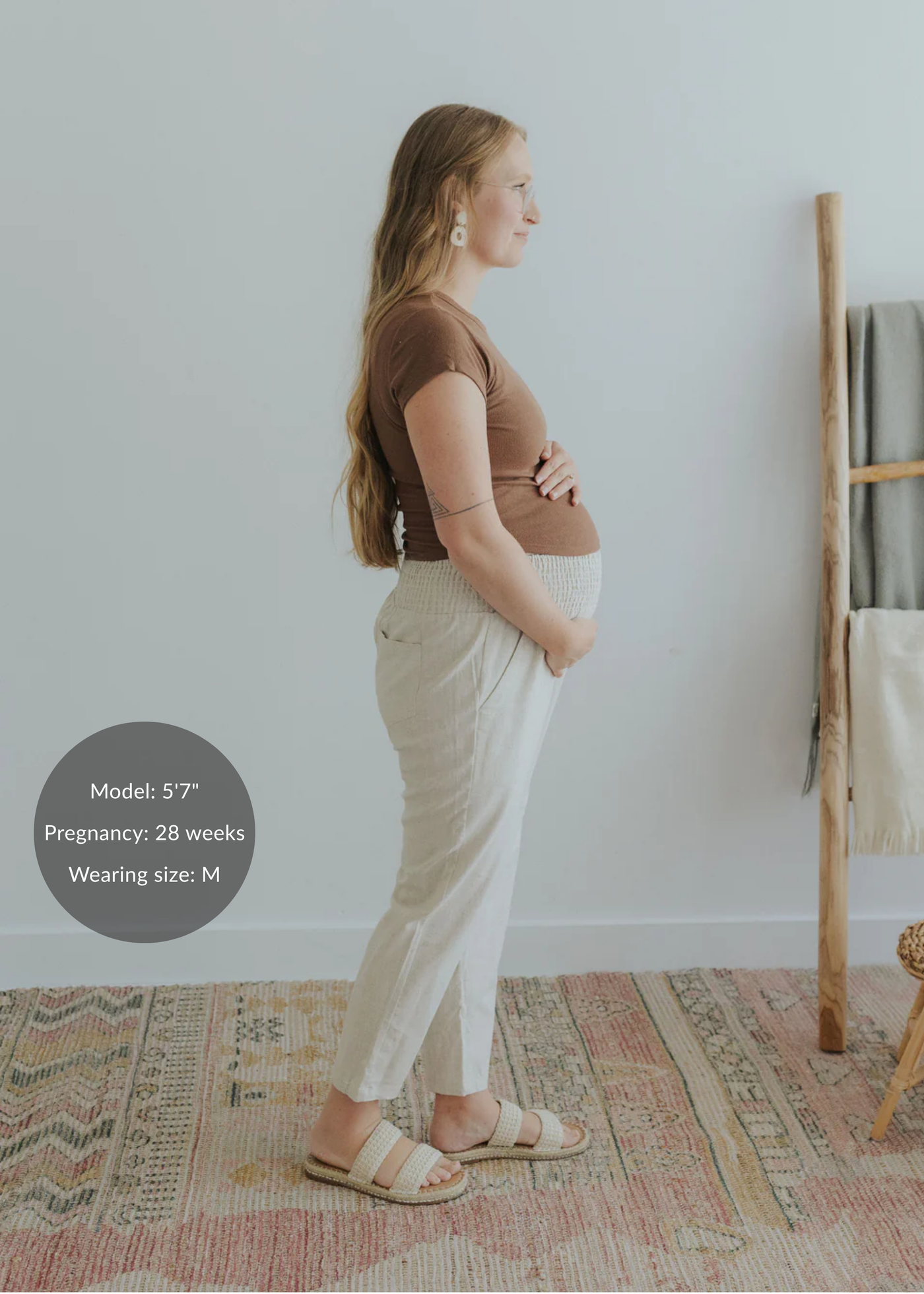 Pregnant model in side profile wearing light beige smocked linen maternity pants with functional pockets.