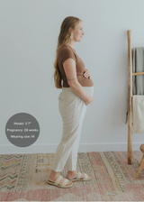 Pregnant model in side profile wearing light beige smocked linen maternity pants with functional pockets.
