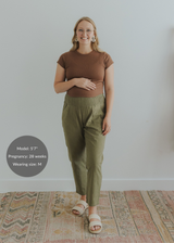 Pregnant model in olive green smocked linen pants, brown top, and cream sandals.