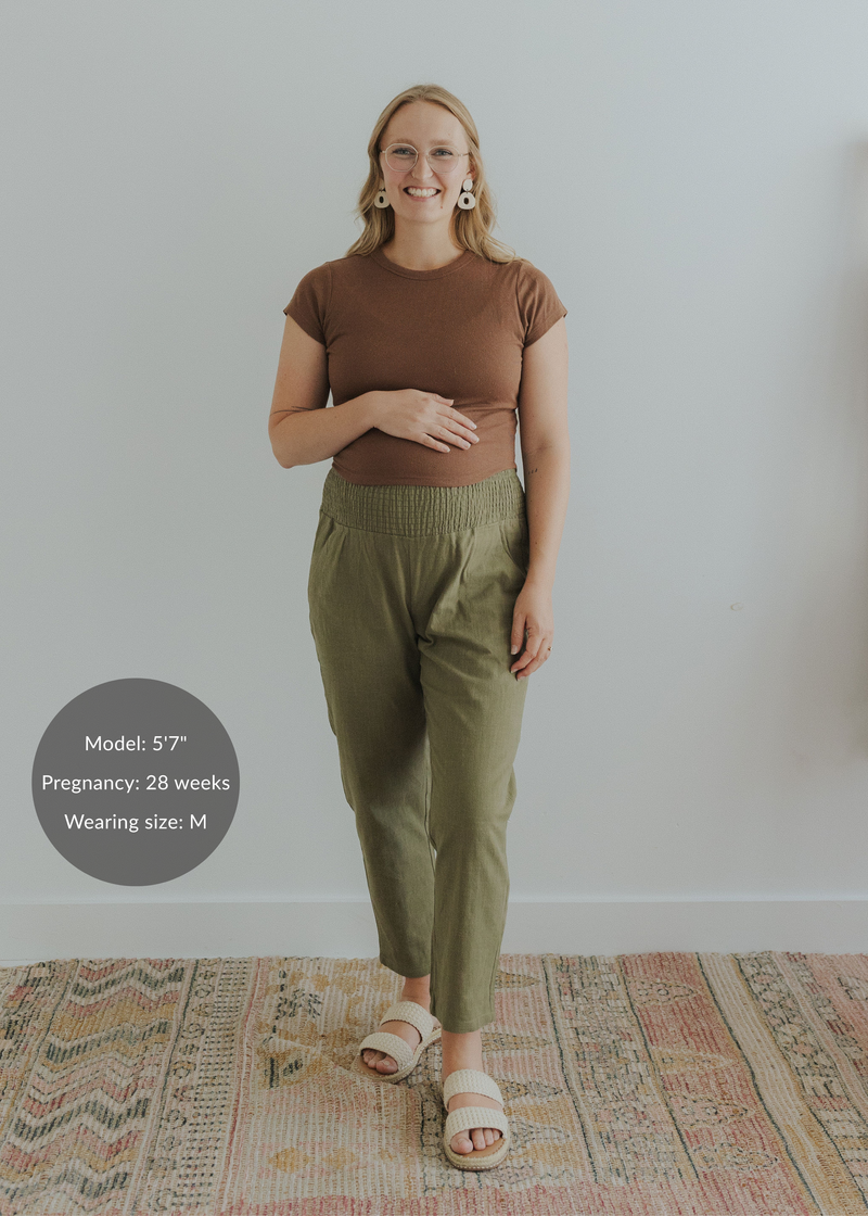 Pregnant model in olive green smocked linen pants, brown top, and cream sandals.