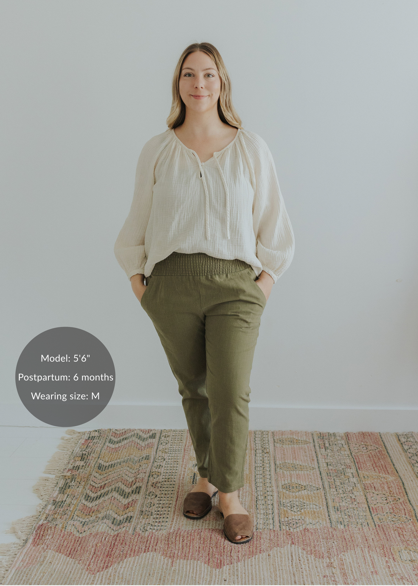 Woman in olive green smocked linen pants and an off-white blouse, hands in pockets.