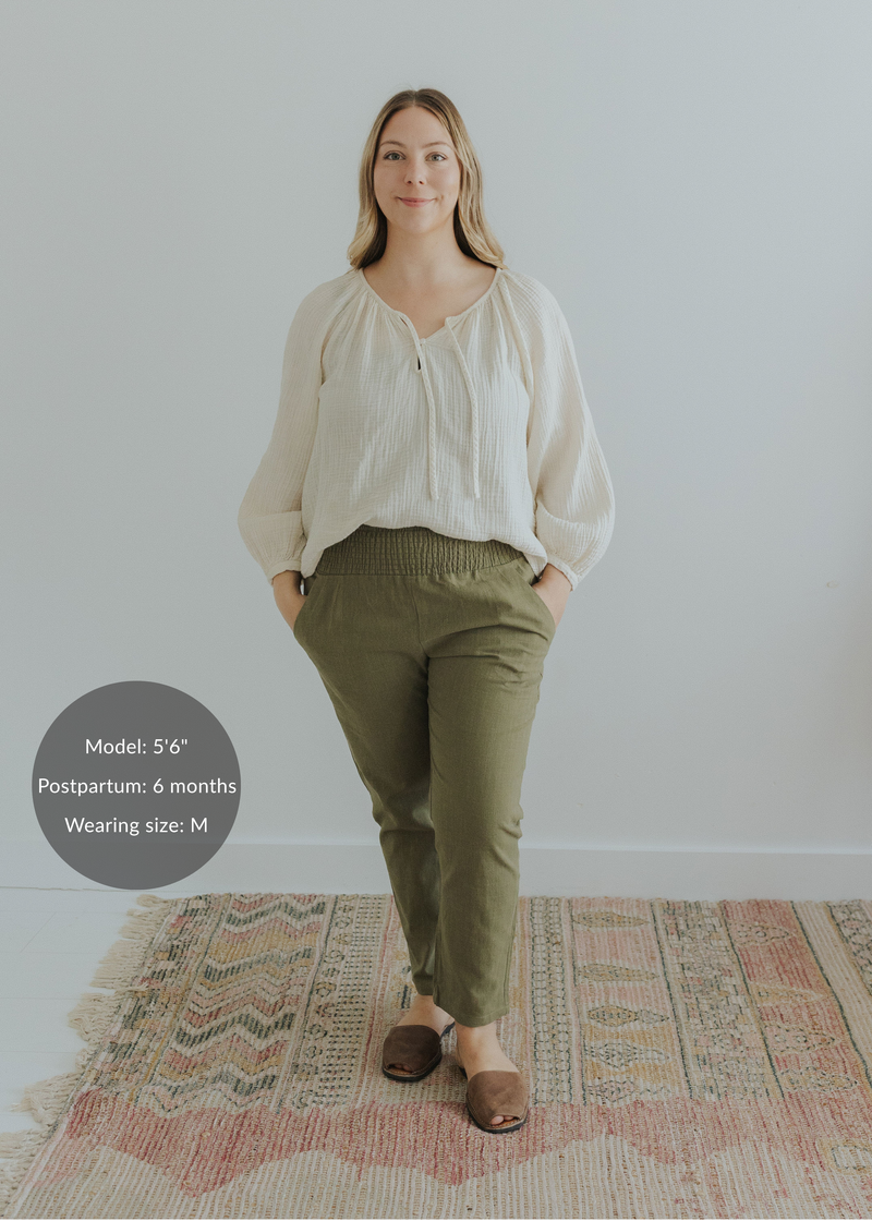 Woman in olive green smocked linen pants and an off-white blouse, hands in pockets.