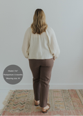 Woman in brown smocked linen pants with pockets and a cream top, seen from behind.