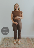 Pregnant woman in brown smocked linen pants and a matching top, holding her belly.