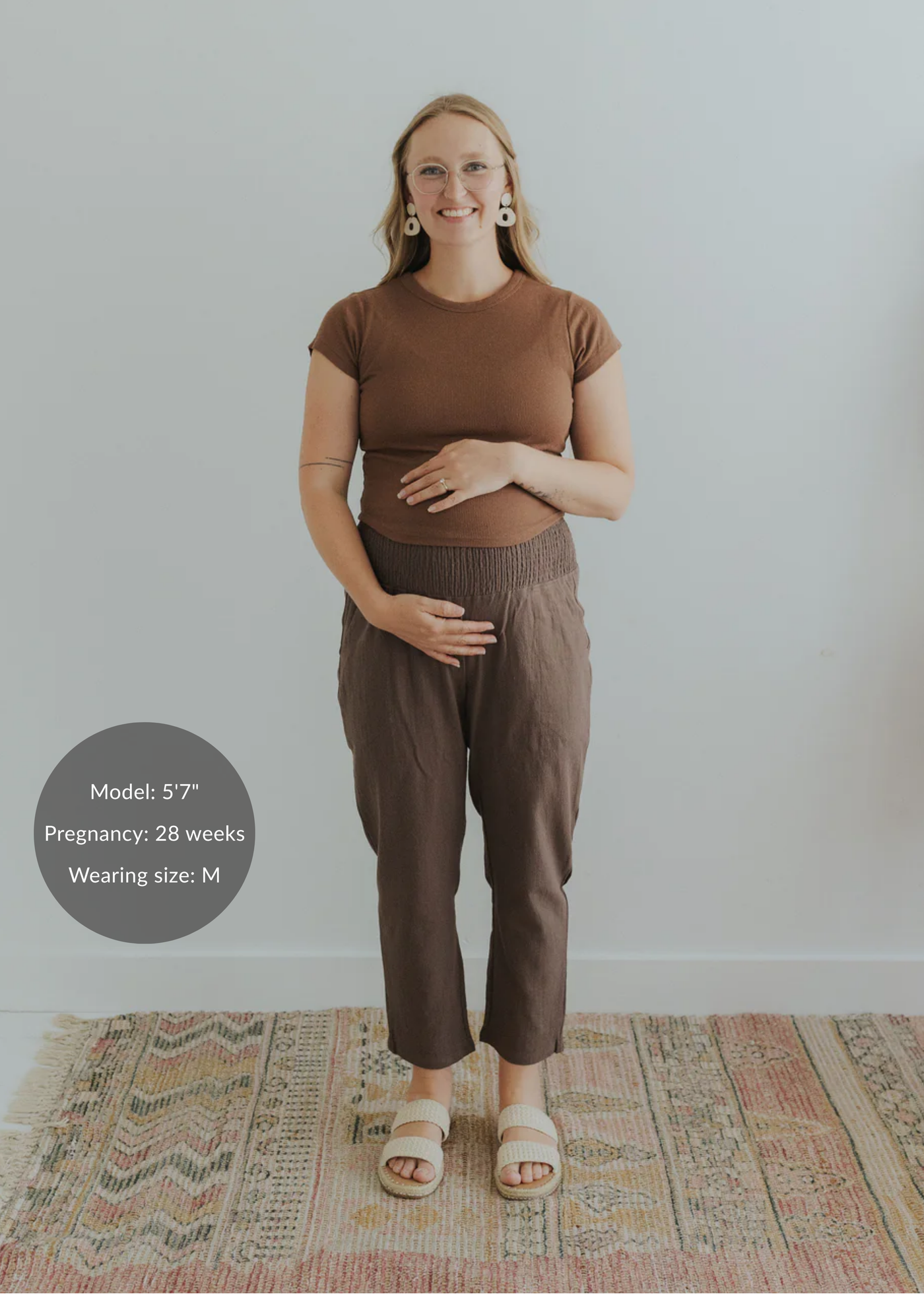 Pregnant woman in brown smocked linen pants and a matching top, holding her belly.