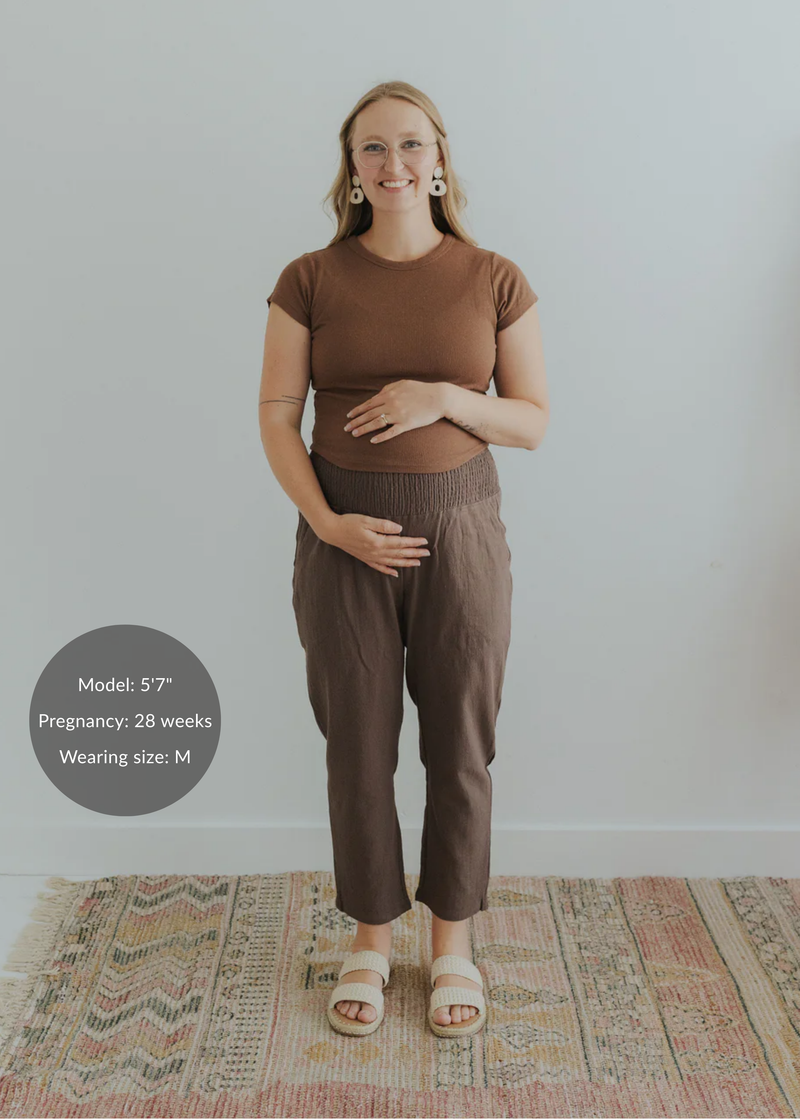 Pregnant woman in brown smocked linen pants and a matching top, holding her belly.