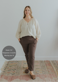 Woman modeling dark brown smocked linen pants with pockets and an ivory blouse.