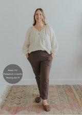 Woman modeling dark brown smocked linen pants with pockets and an ivory blouse.