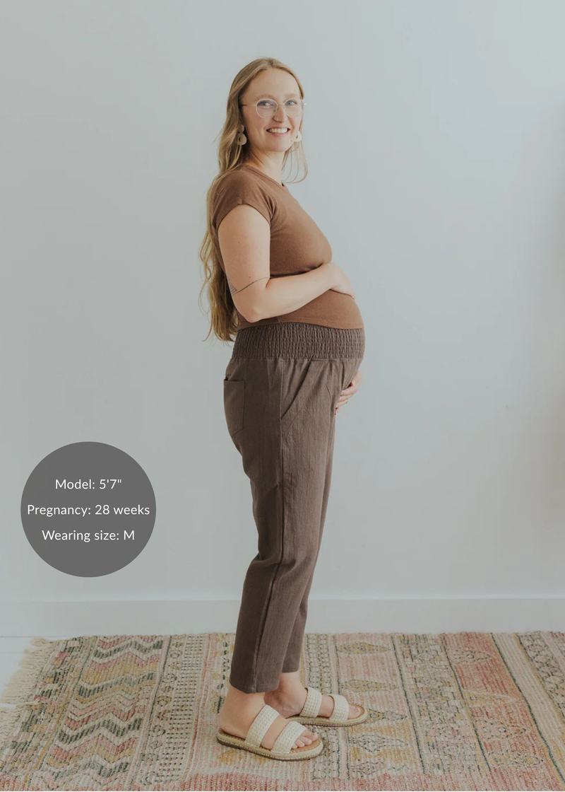 Pregnant woman in brown smocked linen maternity pants with pockets and a matching top.