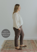 Woman in brown smocked linen pants and cream top, side view, standing on a patterned rug.