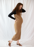 Pregnant woman in a brown linen Beatrice Button Jumpsuit over a black long-sleeve shirt, with brown sandals.