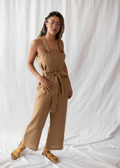 Woman in a Beatrice Button Jumpsuit: a brown linen, wide-leg jumpsuit with a tie waist and button straps.