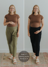 Blonde woman wearing a brown top, modeling olive green and black linen maternity pants with smocked waist and pockets.