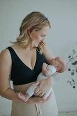 Woman holding her baby in the Black Crossover Sleep Bra, front view