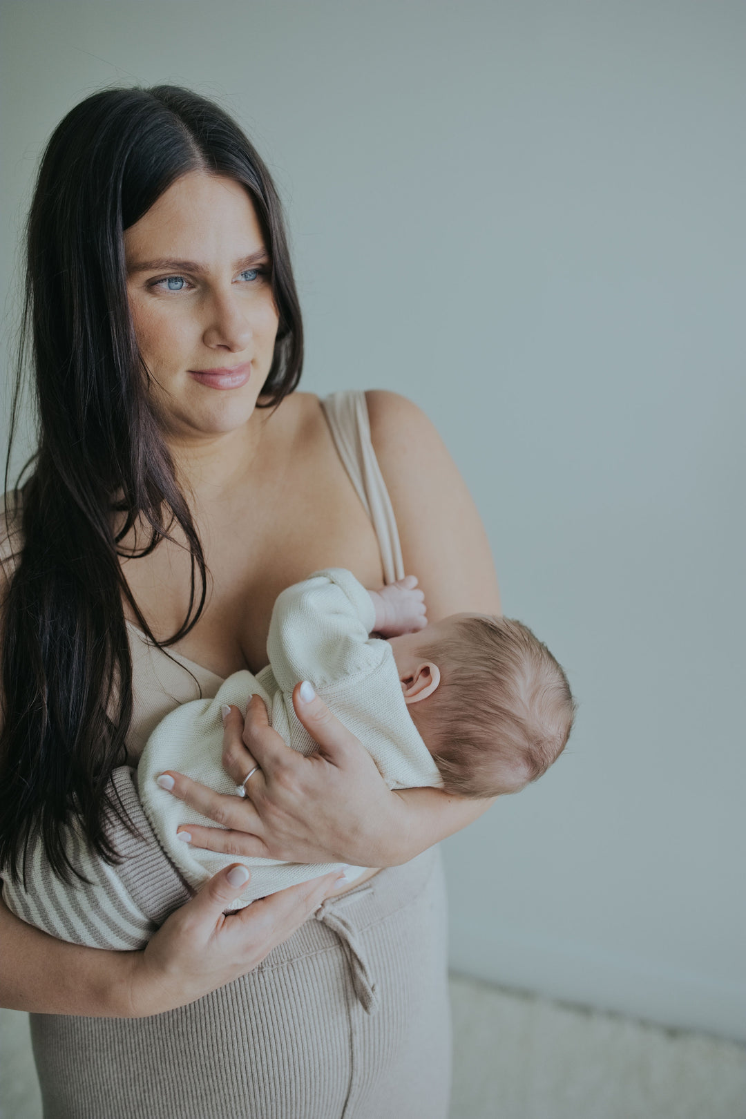 Woman holding her baby in the Sand Crossover Sleep Bra, close front view