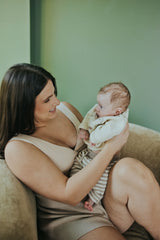 Woman holding her baby in the Sand Crossover Sleep Bra, seated